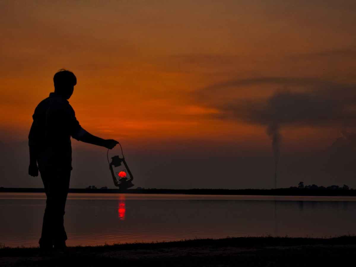 silhouette of man with oil lamp on shore at sunset